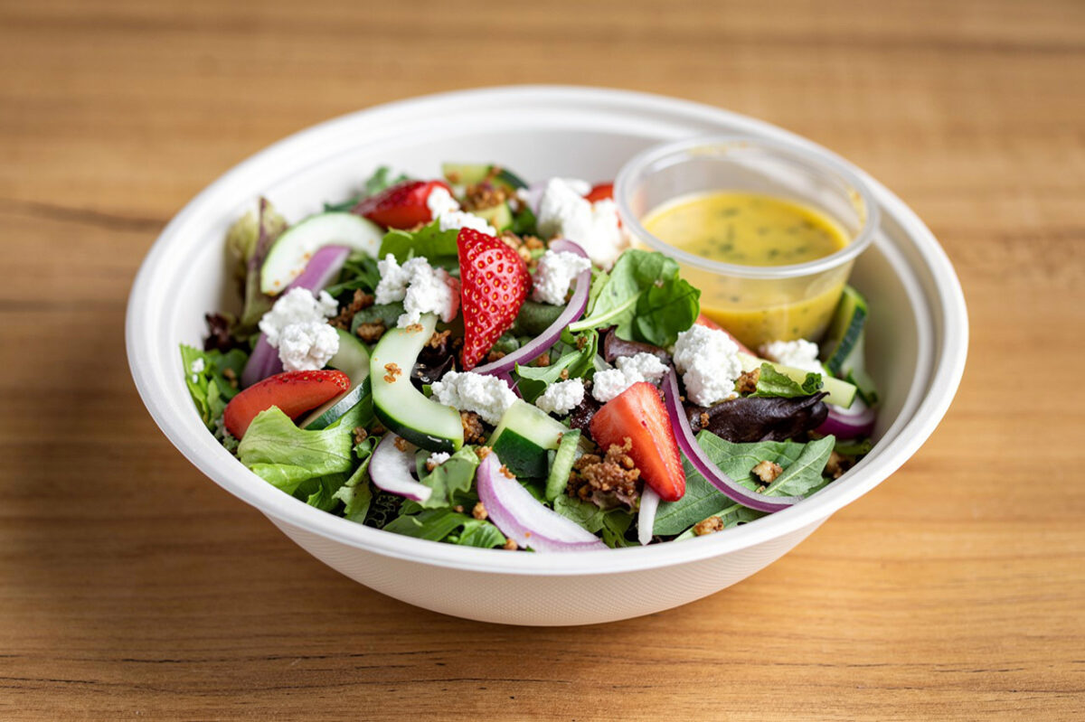a vibrant salad in a white bowl, showcasing strawberries, crisp lettuce, and creamy cheese.